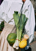 Woman holding a black net bag called Ida over her shoulder full of vegetables.